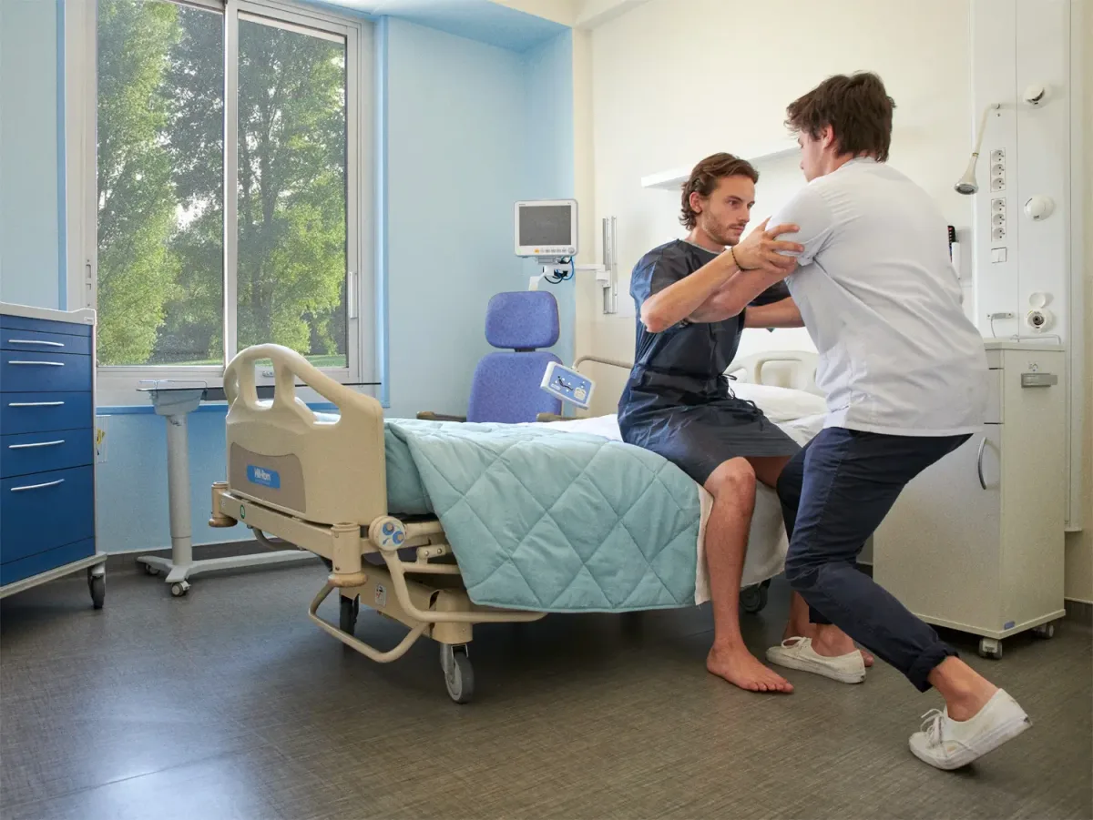 Photo of a physiotherapist helping a patient to stand after a disc replacement surgery