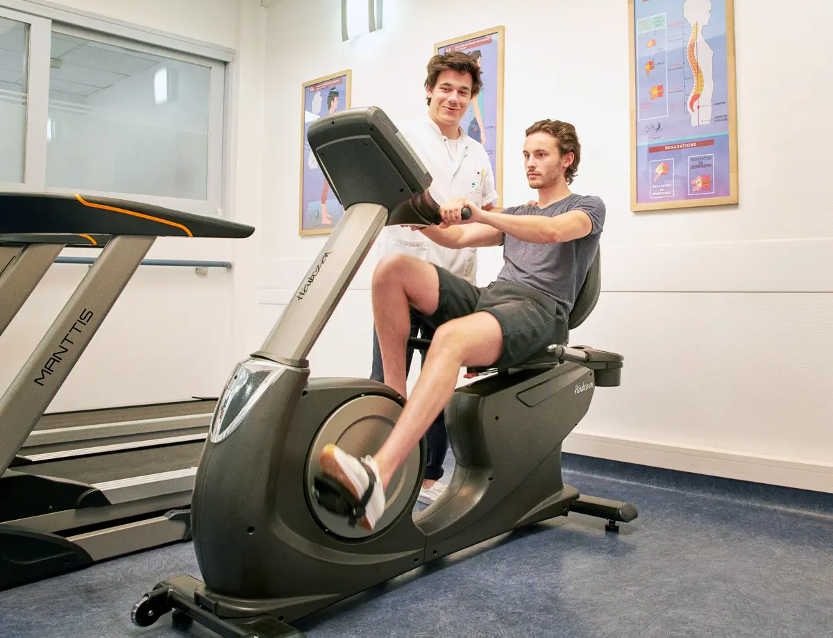 A patient on an exercise bike with a physiotherapist beside him