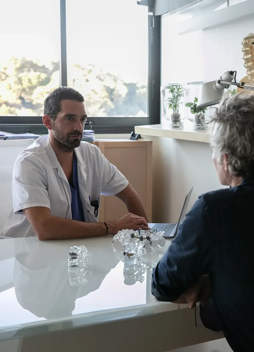 A doctor with a patient explaining a disc replacement procedure with some models on the desk